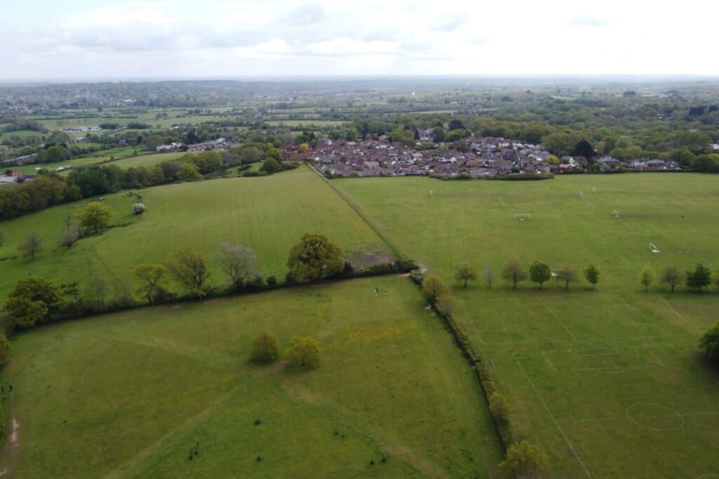 Fields and hedgerows meeting the edge of a housing estate, the kind of boundary the Green Belt is drawn to protect