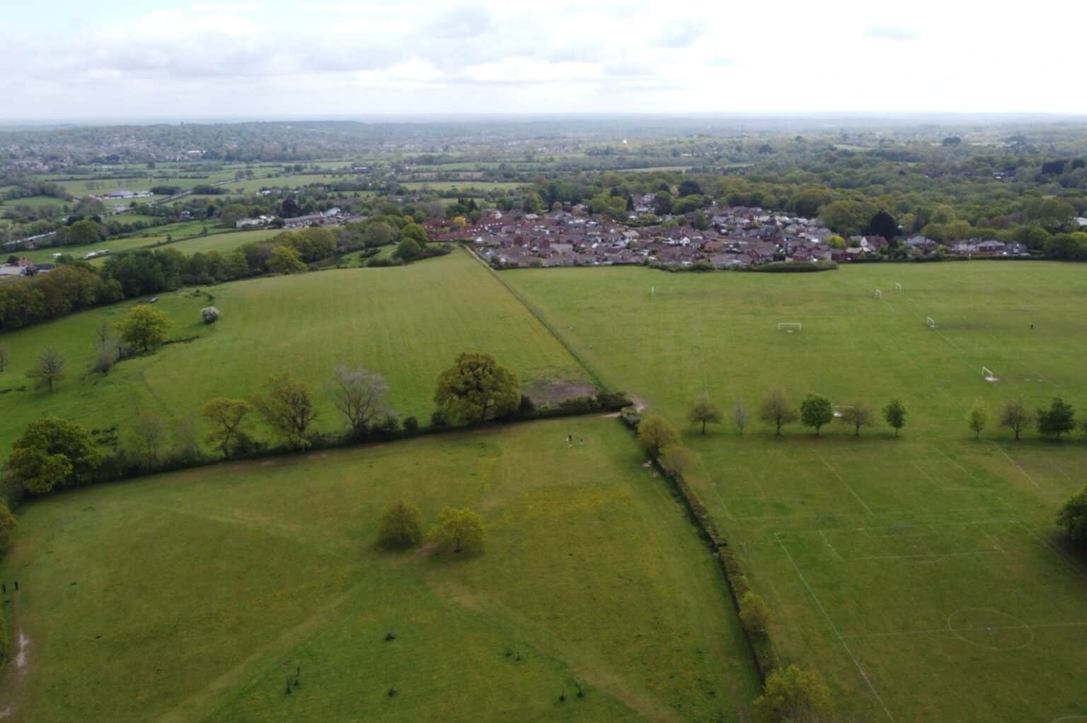 Fields and hedgerows meeting the edge of a housing estate, the kind of boundary the Green Belt is drawn to protect