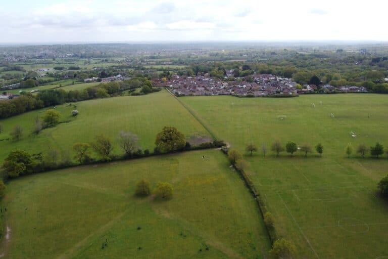 Fields and hedgerows meeting the edge of a housing estate, the kind of boundary the Green Belt is drawn to protect