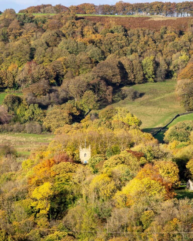 Eyam village and its church tower among autumn woodland in the Derbyshire Dales